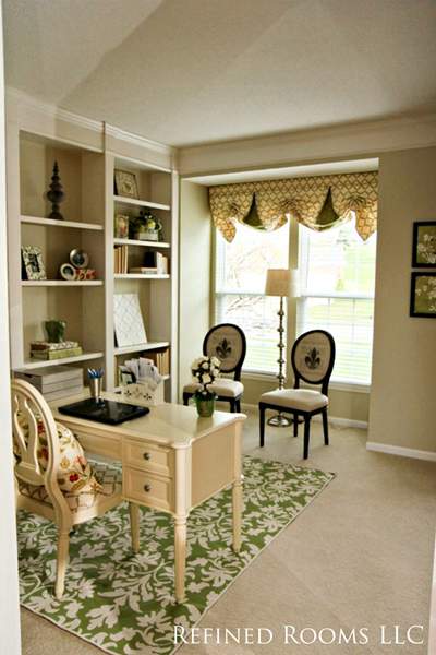 decorated home office with a bay window and built in bookshelves.