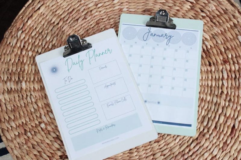 monthly calendar printable and daily planner printable on clipboards sitting on a table.