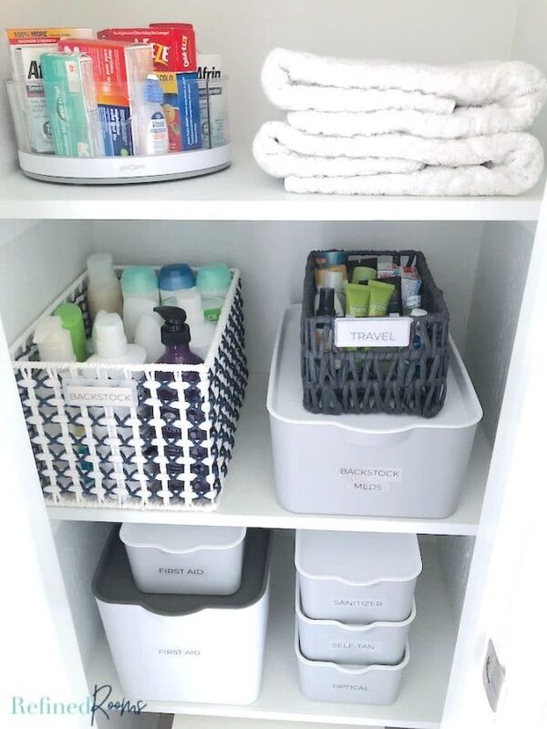 an organized bathroom closet with labeled bins and baskets.